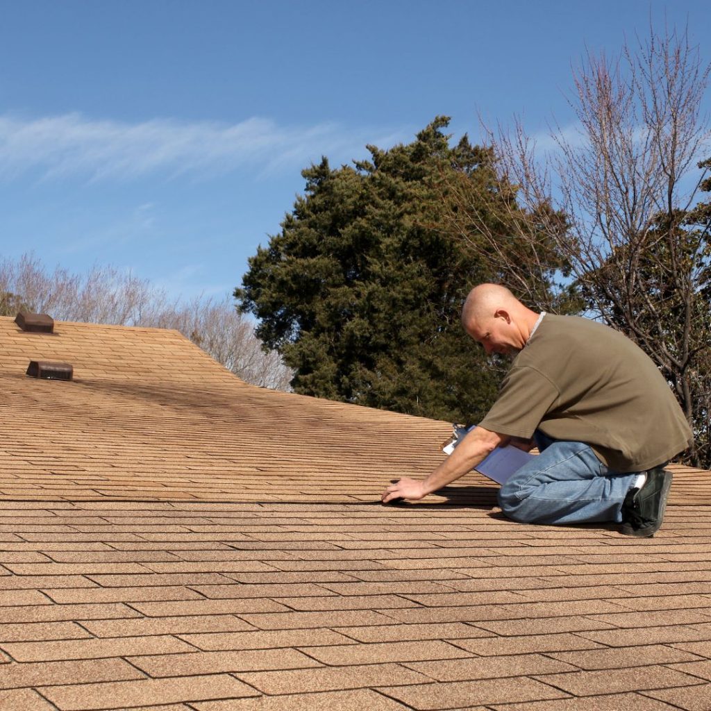 Man kneeling doing diy roof maintenance on a brown shingle roof