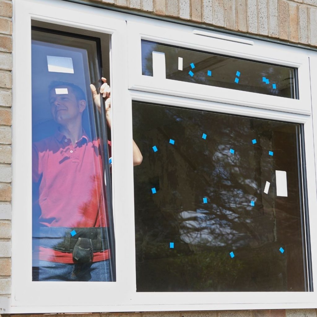 contractor in red shirt installing energy efficient window replacement on home