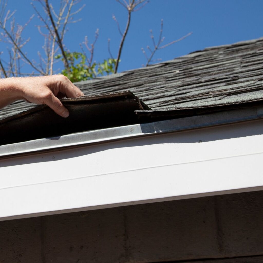 hand listing shingles on edge of house for roof inspection